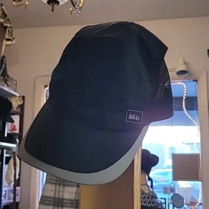 A hat hanging on the wall in front of a mirror.