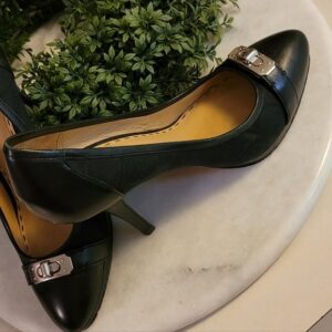 Black high-heeled shoe with metallic accent on a marble surface.