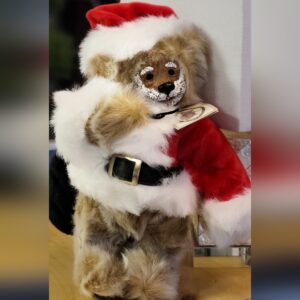 A dog dressed in a Santa Claus costume hugging a stuffed animal.