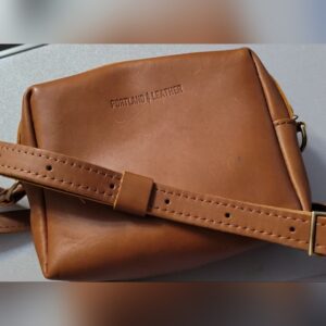 Brown leather crossbody bag with adjustable strap on a white surface.