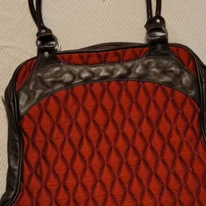 Red and black patterned handbag with leather straps and detailing.