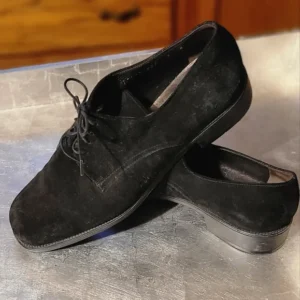 Black suede oxford shoes with laces on a gray surface.