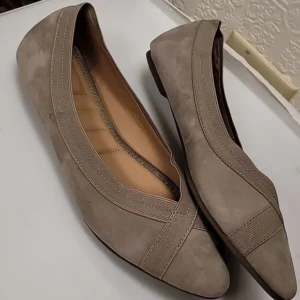 Pair of beige women's flat shoes on a white surface.