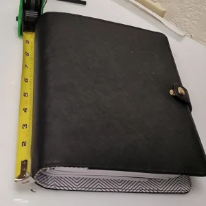 A closed black leather binder with a measuring tape beside it.